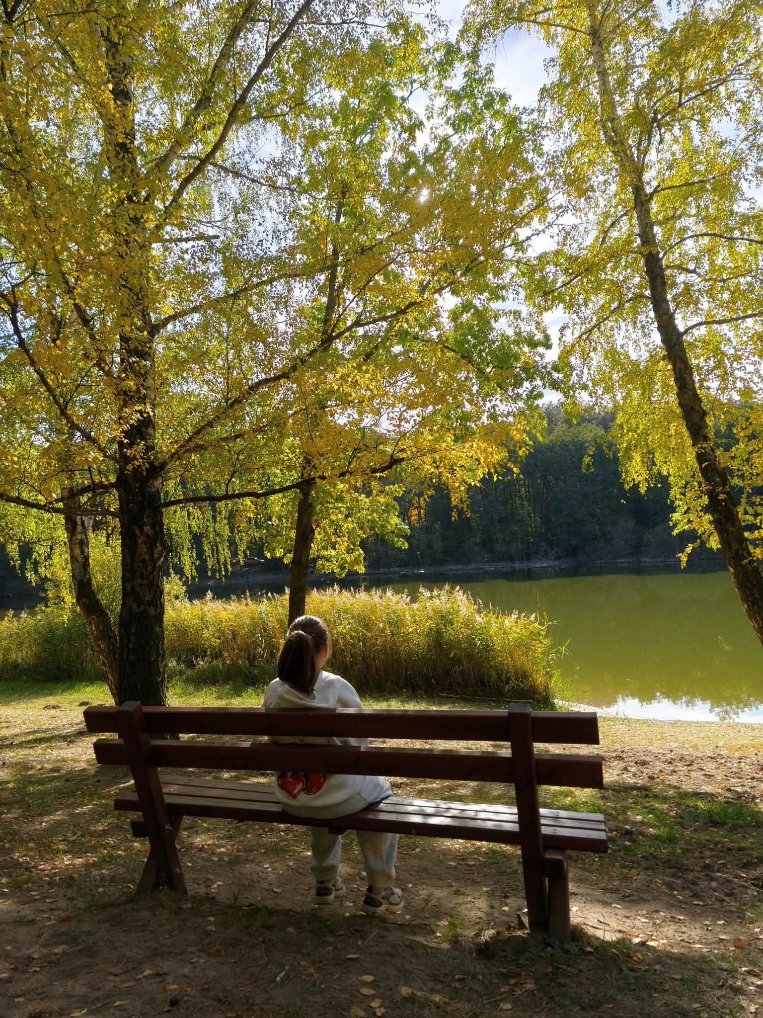 Lulu egy padon ül az őszi tóparton.